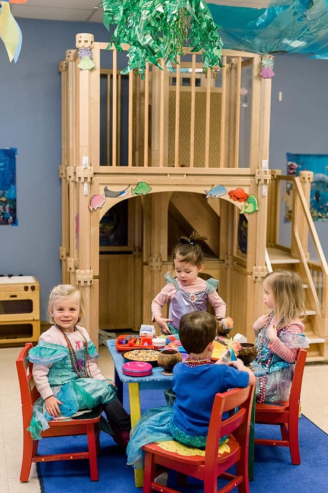 Children in costumes sitting at a small table in a play area