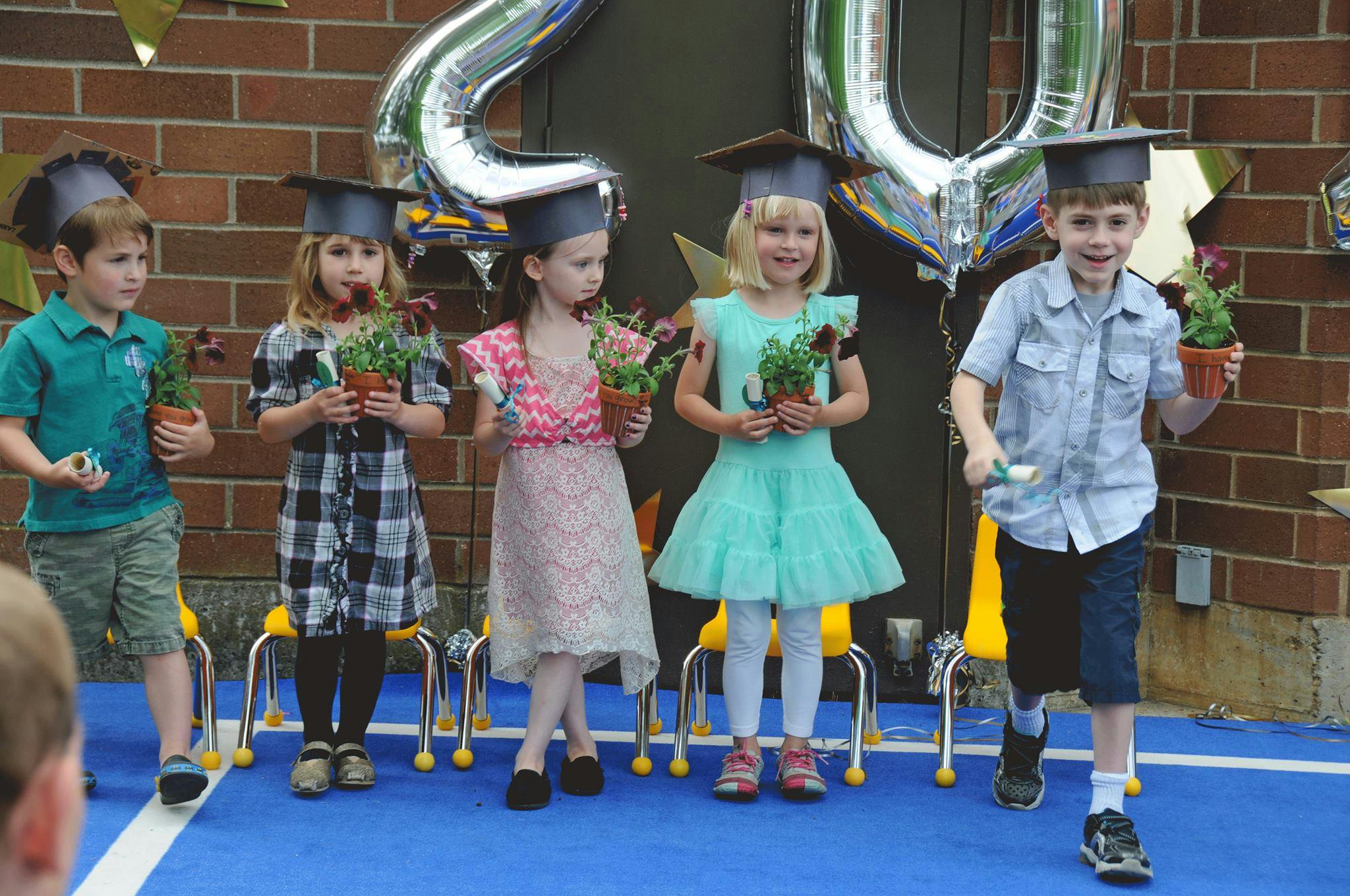 Children in graduation caps holding potted plants