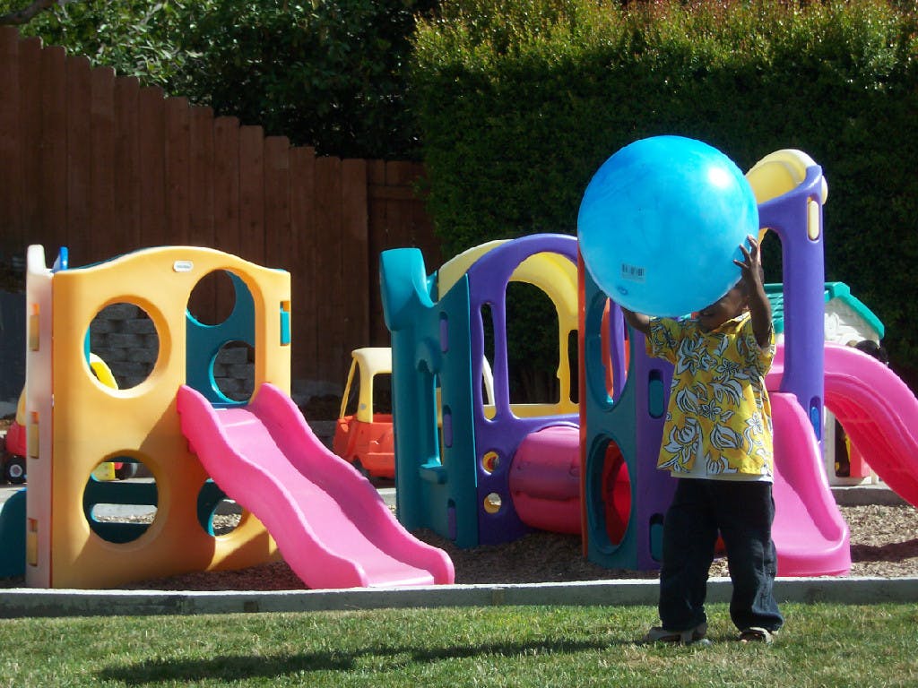 Child holding a large blue ball on a playground
