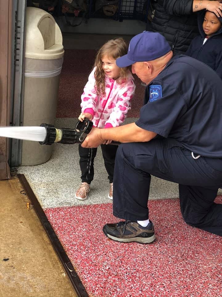 Adult in uniform helping a child hold a fire hose spraying water