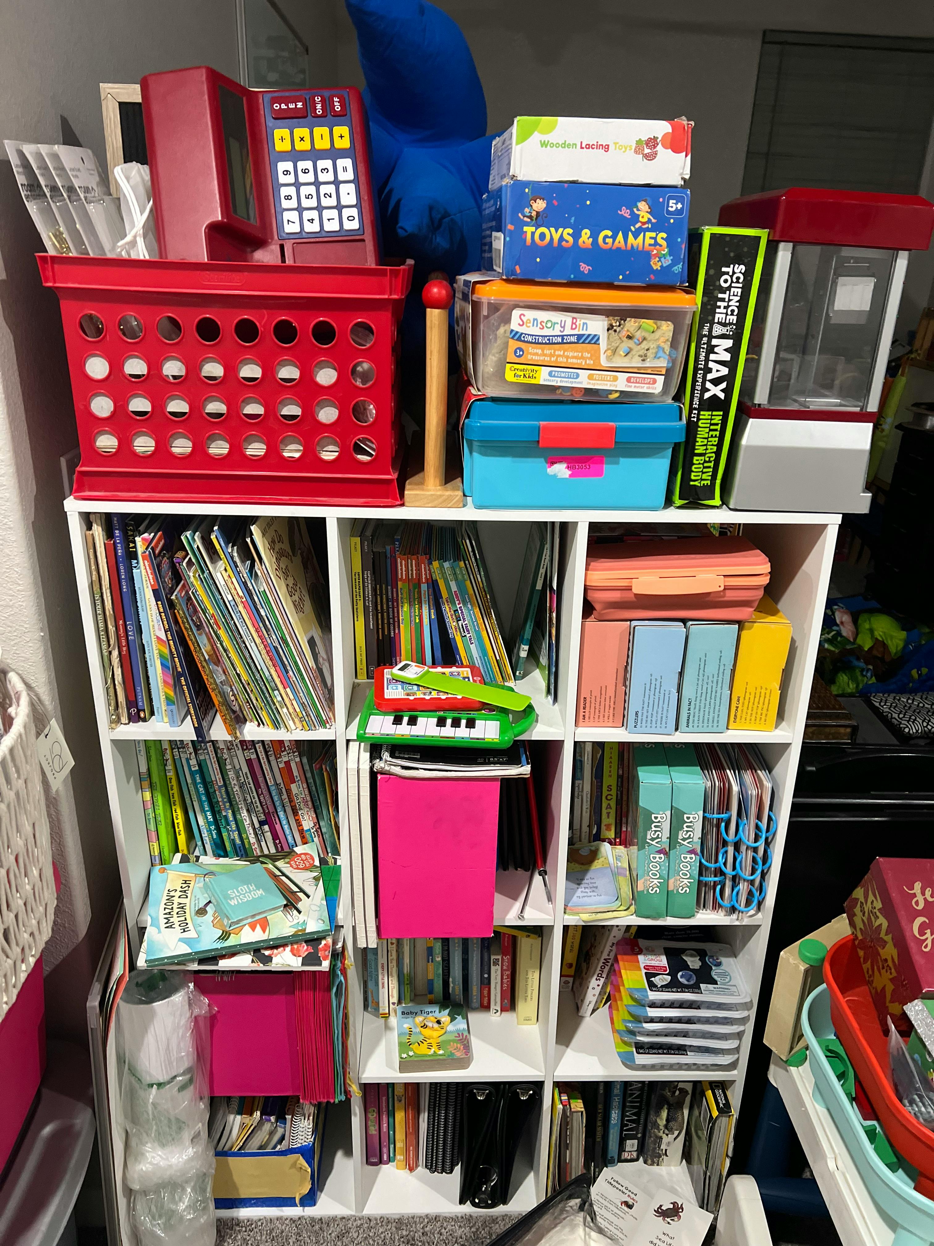 White cubby shelf filled with books, toys, and various containers
