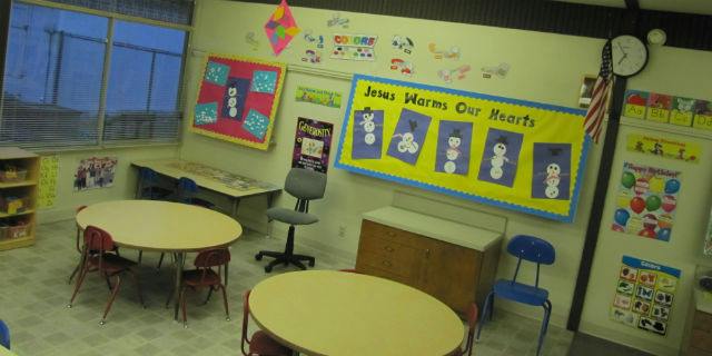 Empty classroom with small tables and chairs, and bulletin boards on the wall