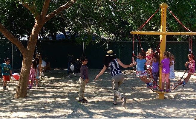 Person interacting with children on a playground merry-go-round