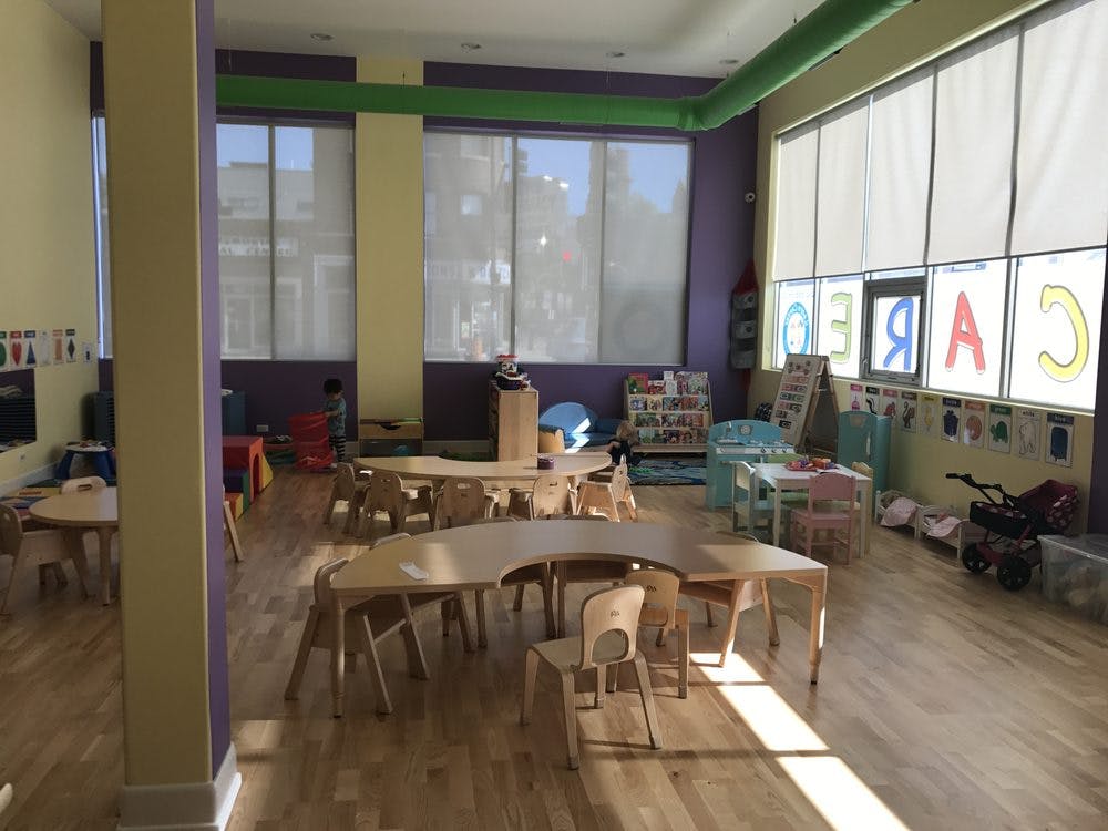 Classroom with small tables and chairs, large windows with shades
