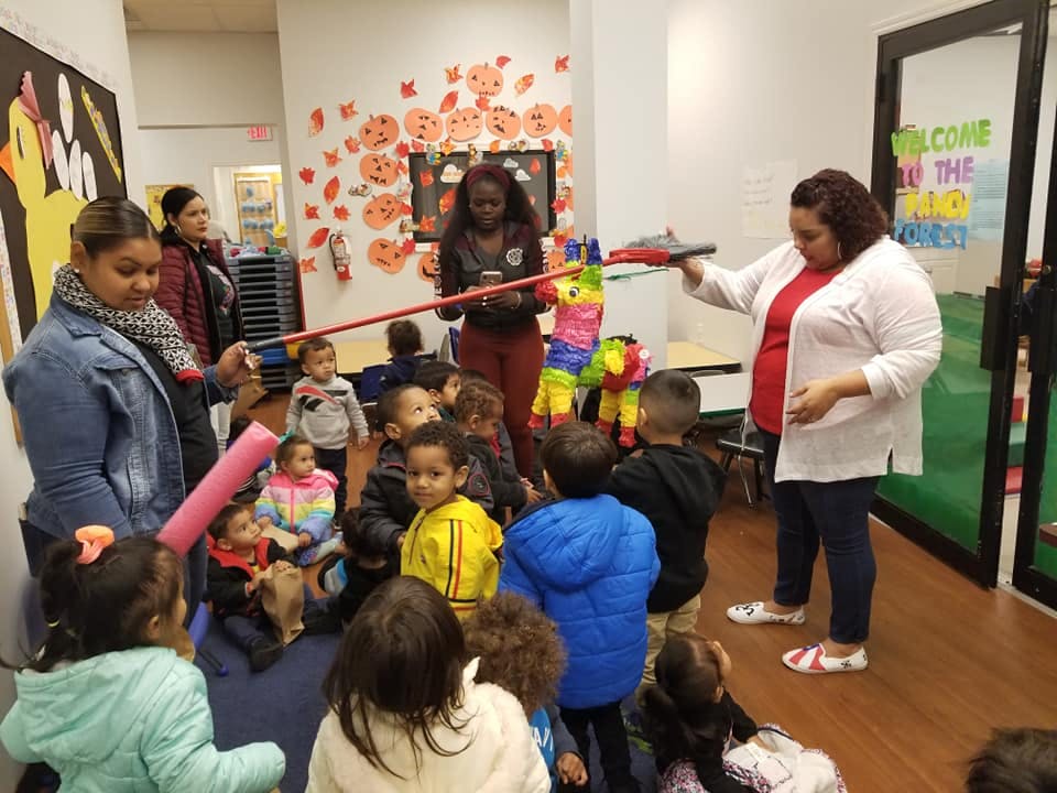 Adults and children gathered around a colorful piñata in a classroom