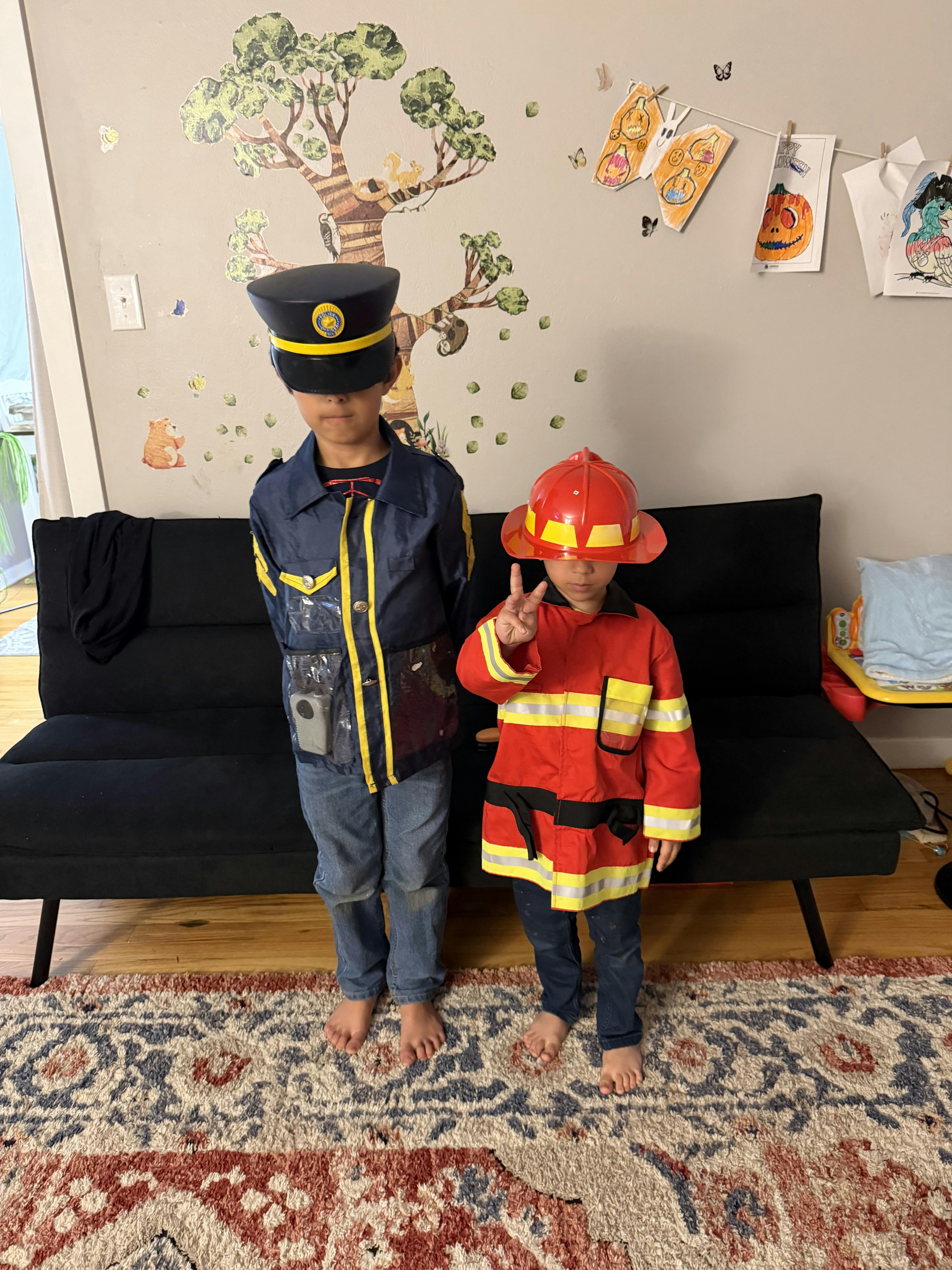 Two children wearing police and firefighter costumes standing by a couch