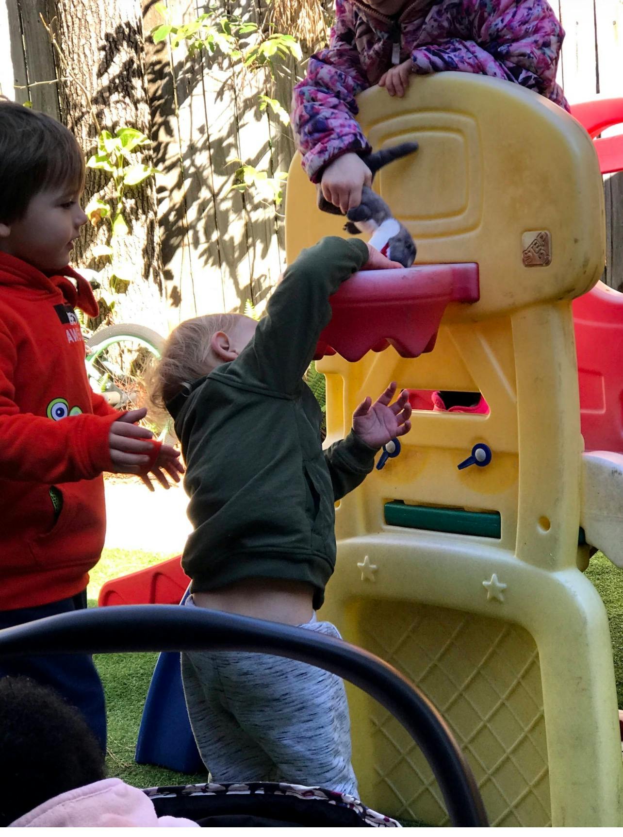 Children playing with a toy on a plastic basketball hoop in a yard
