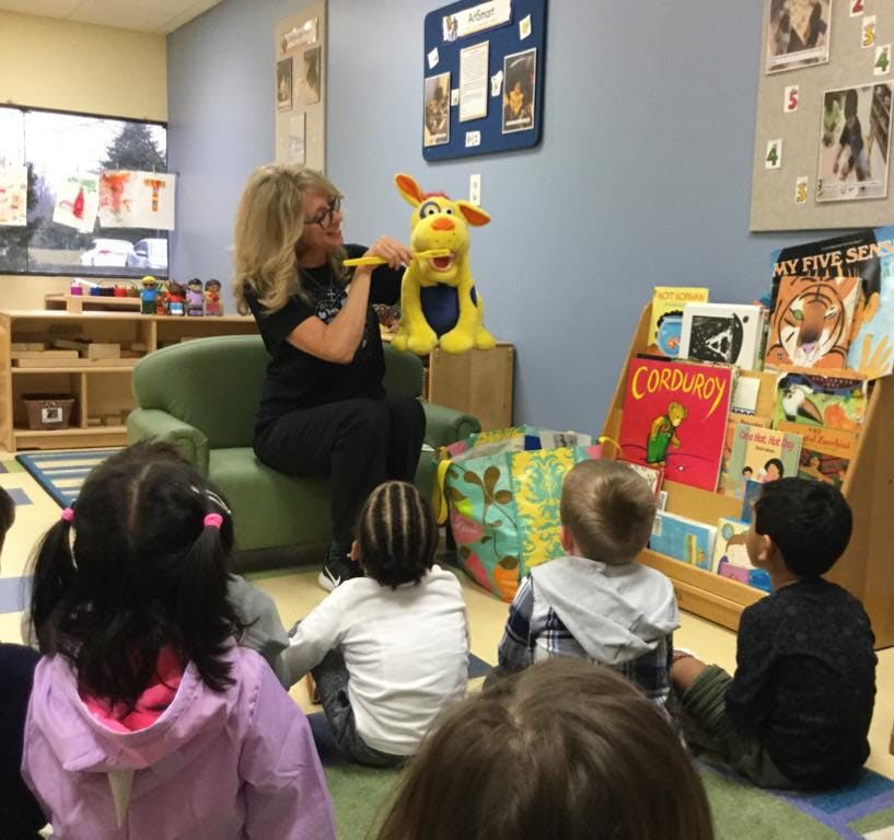 Person sitting in a chair with a puppet, speaking to children on the floor