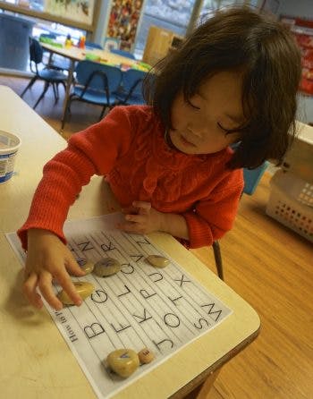 Child placing rocks with letters on an alphabet sheet in a classroom