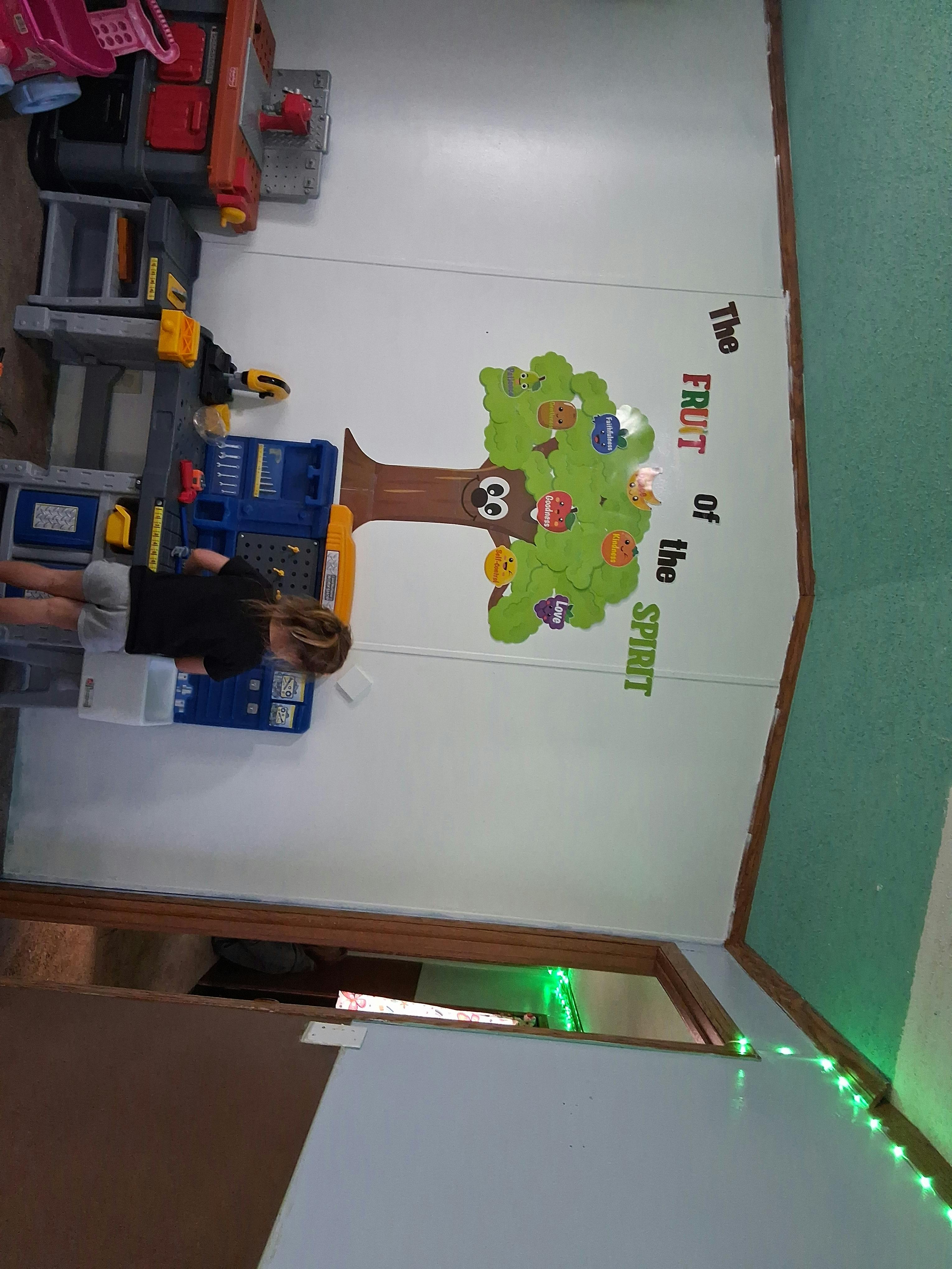 Child standing next to a toy workbench with a tree wall decal