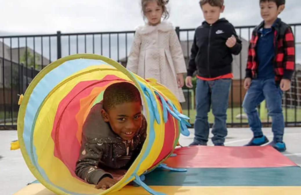 Child crawling through a colorful play tunnel with other children standing nearby