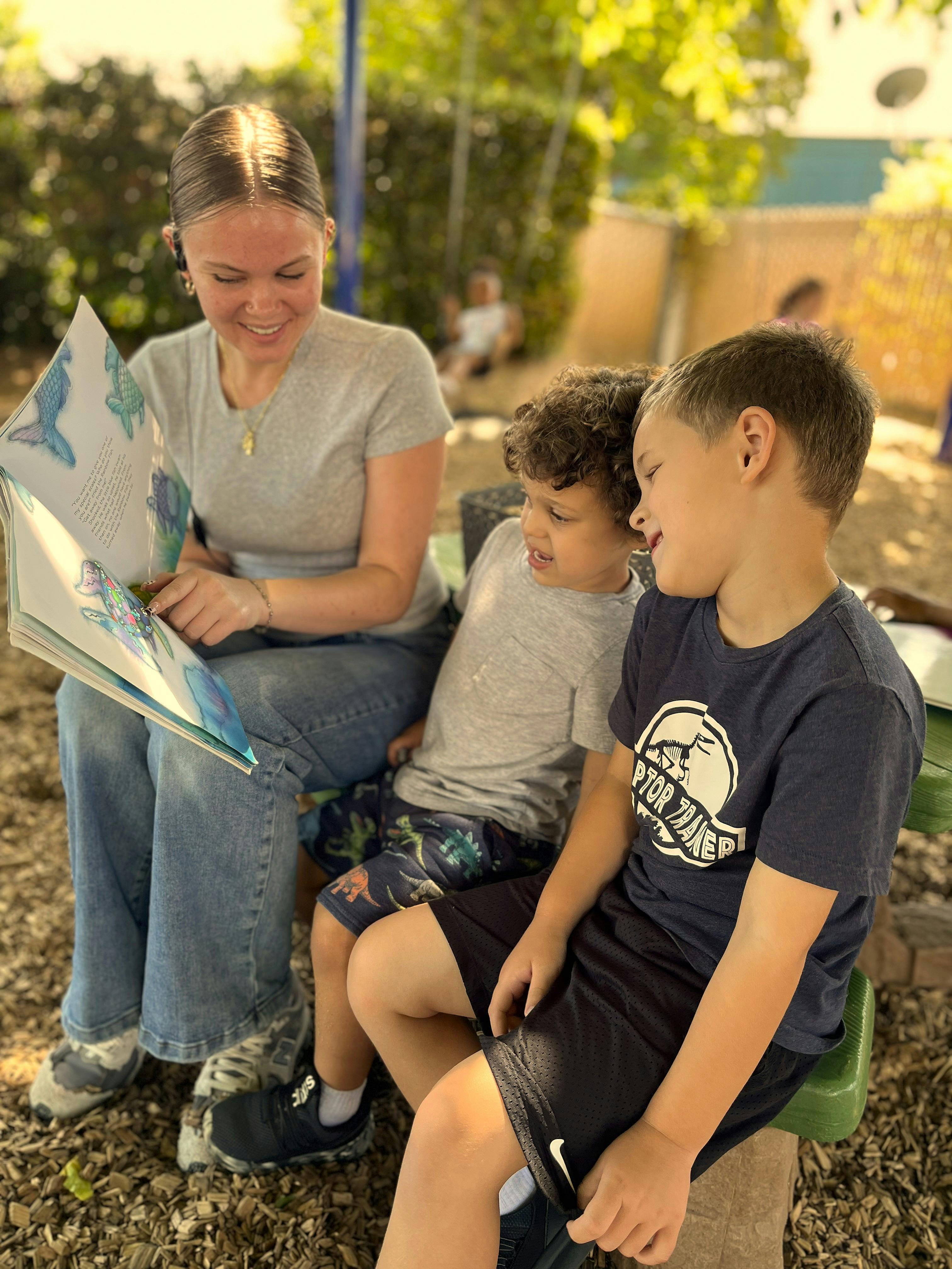 A person reading a book to two children outdoors