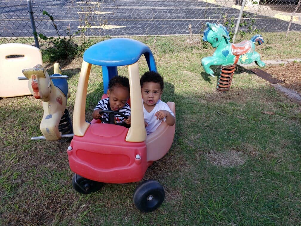 Two children in a toy car on grass