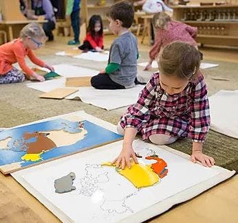 Child assembling a puzzle on the floor with other children in the background