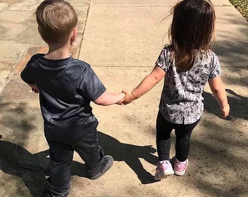Two children holding hands and walking away