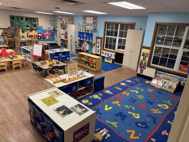 A colorful empty classroom with toys, tables, chairs, and an alphabet rug