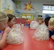 Children blowing into plastic bags in a classroom