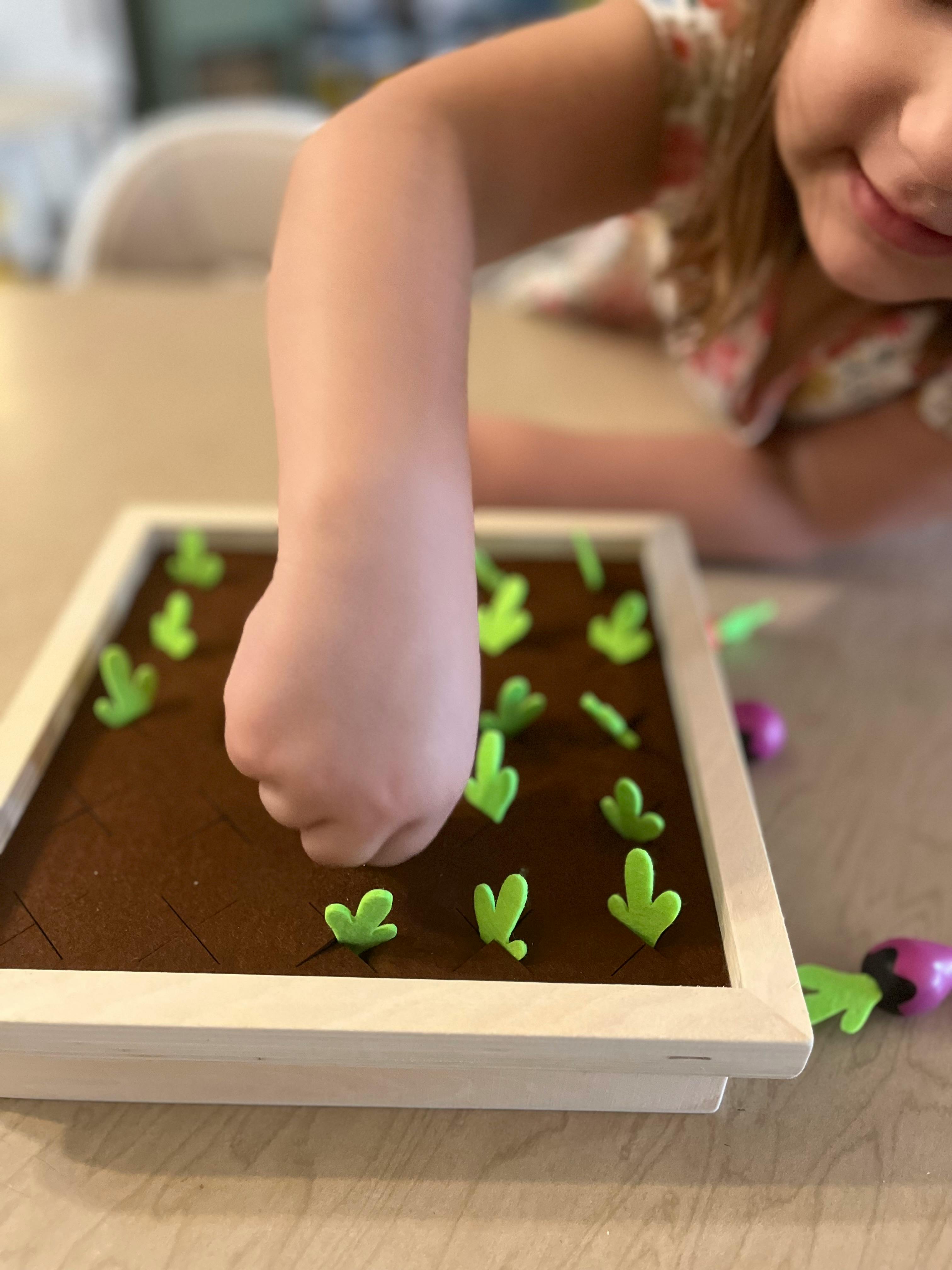 Child's hand reaching into a toy garden with green sprouts