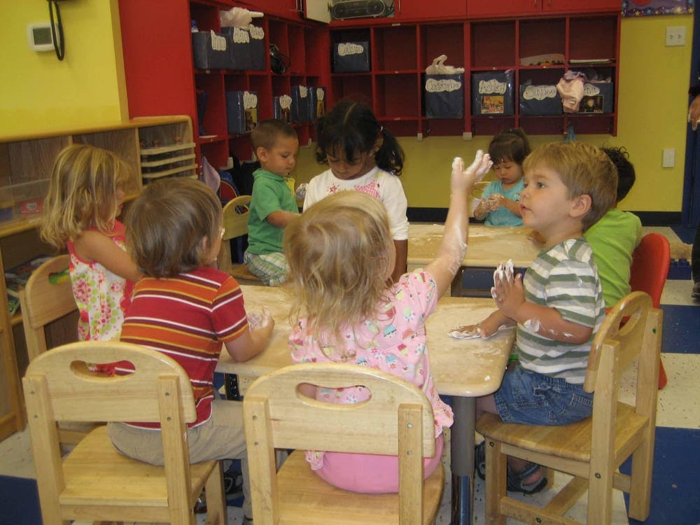 Children sitting at tables in a classroom, some with paint on their hands