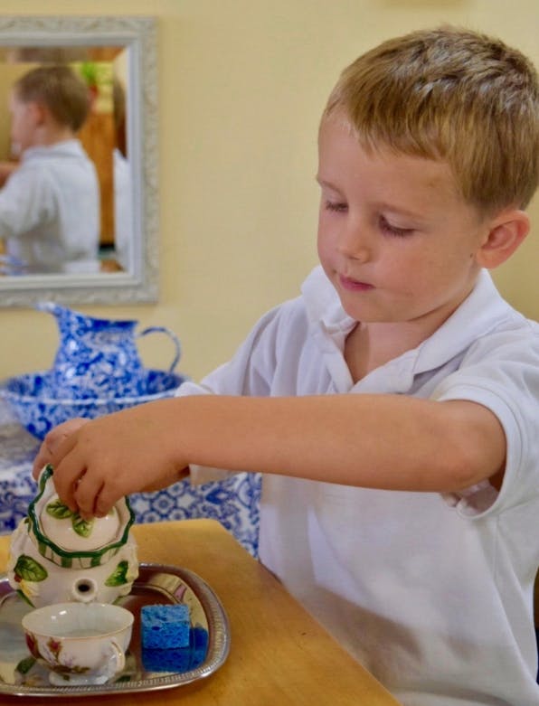Child pouring from a small teapot into a cup