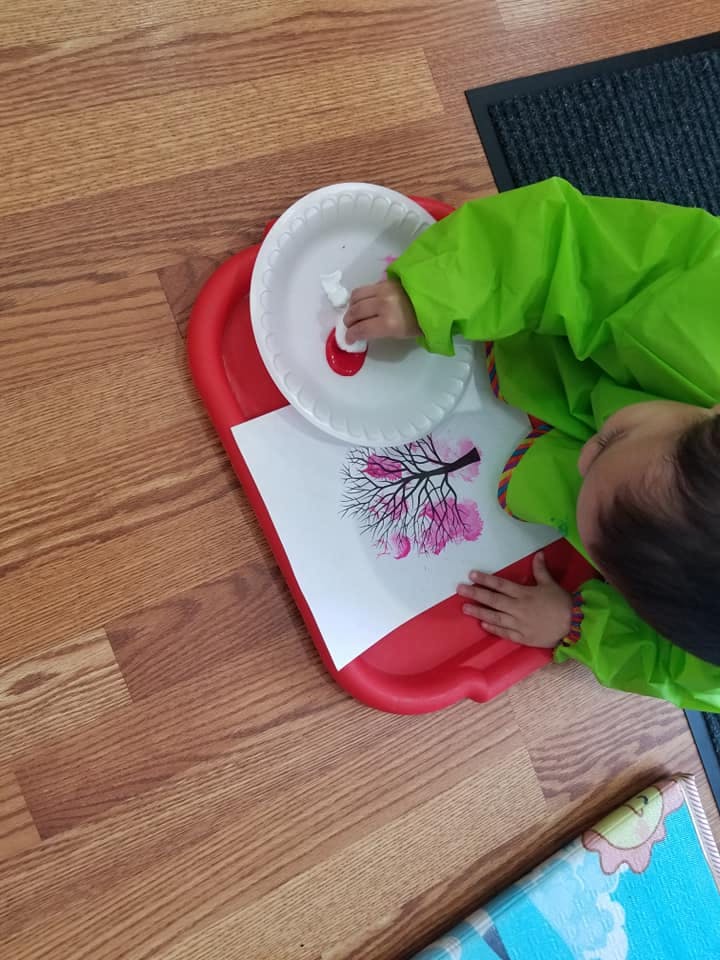 Child in green smock painting a tree with pink blossoms