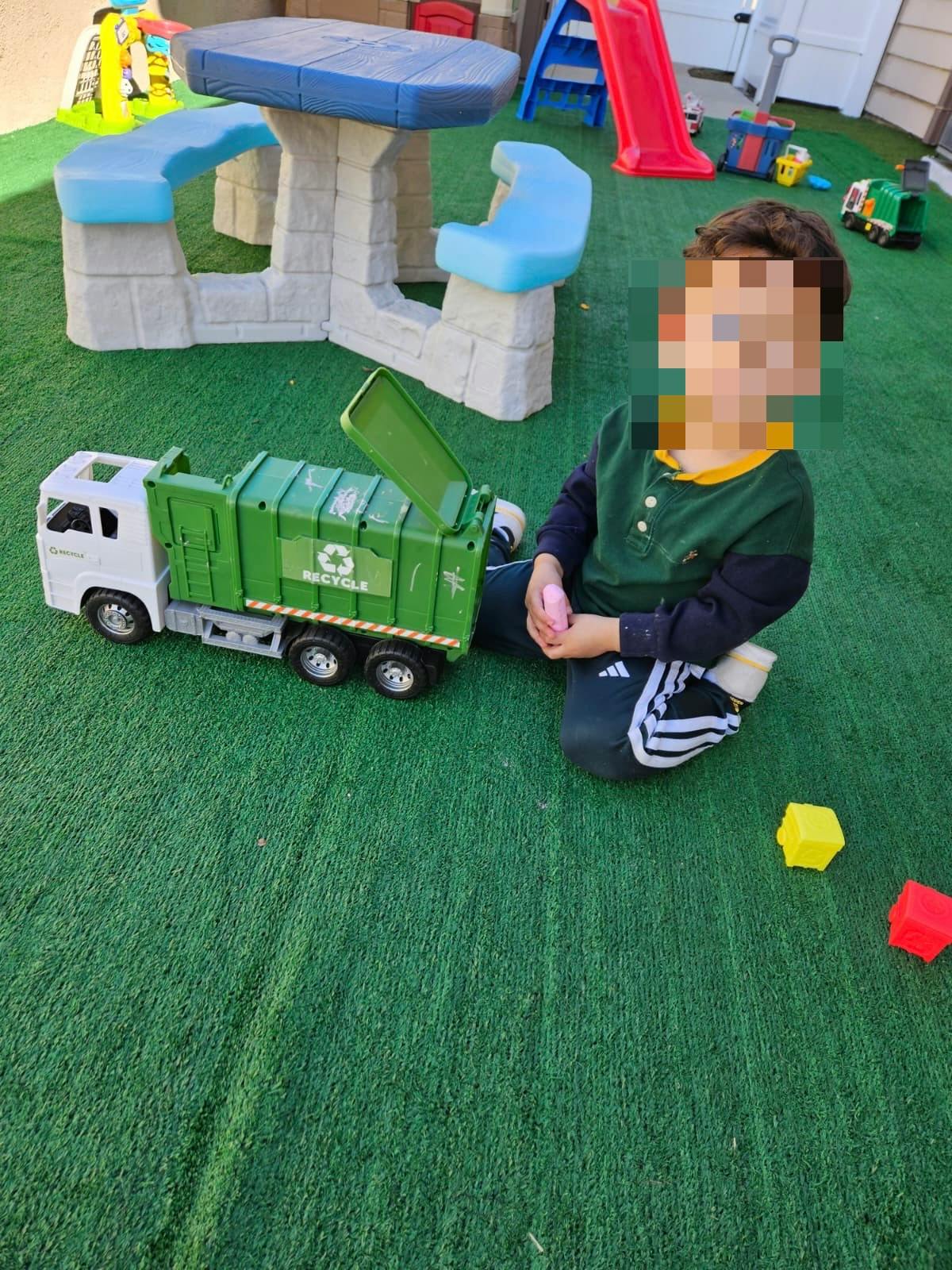 Child kneeling on green turf next to a toy recycling truck