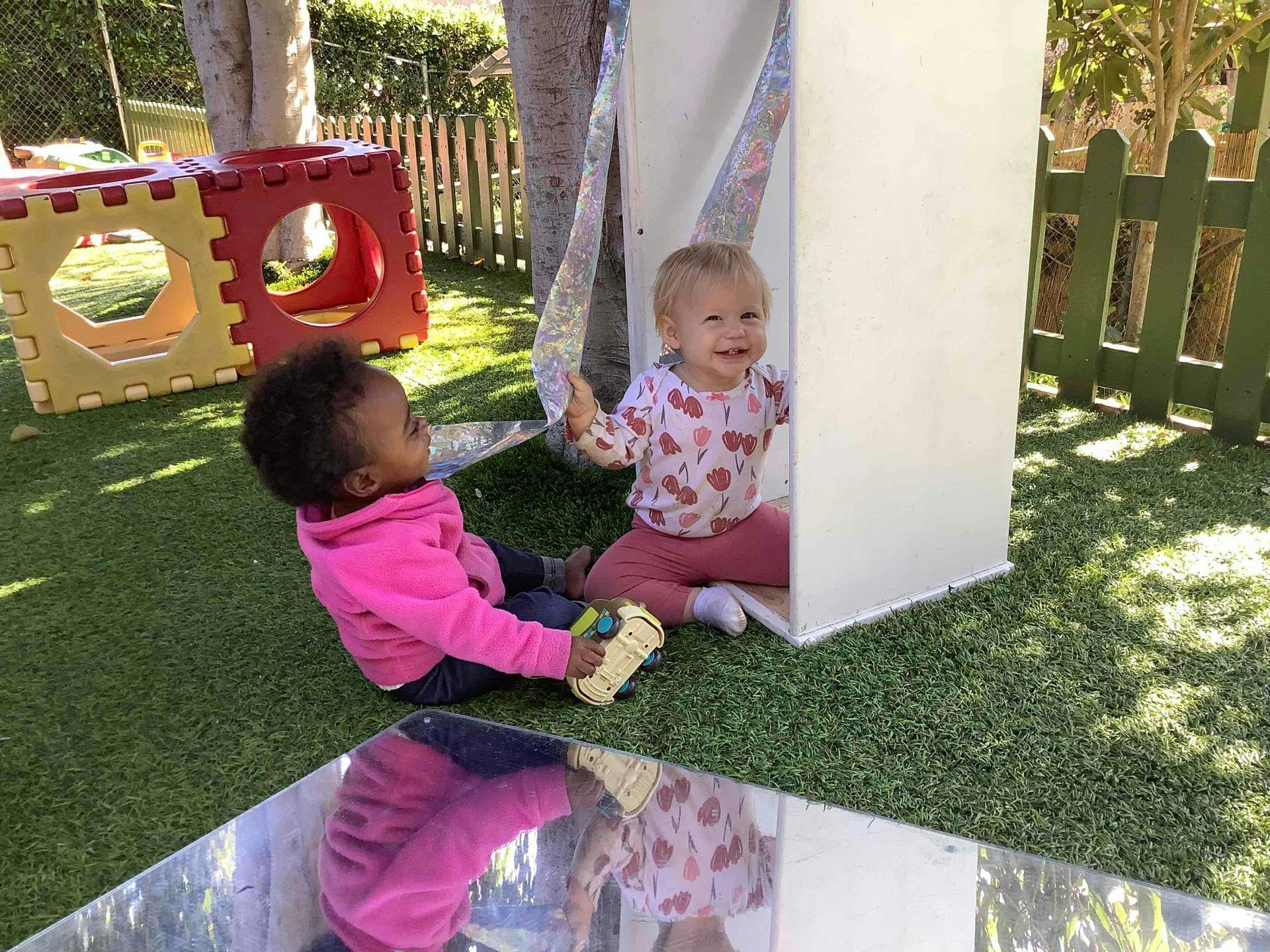 Two children playing on artificial grass, one in a white play structure