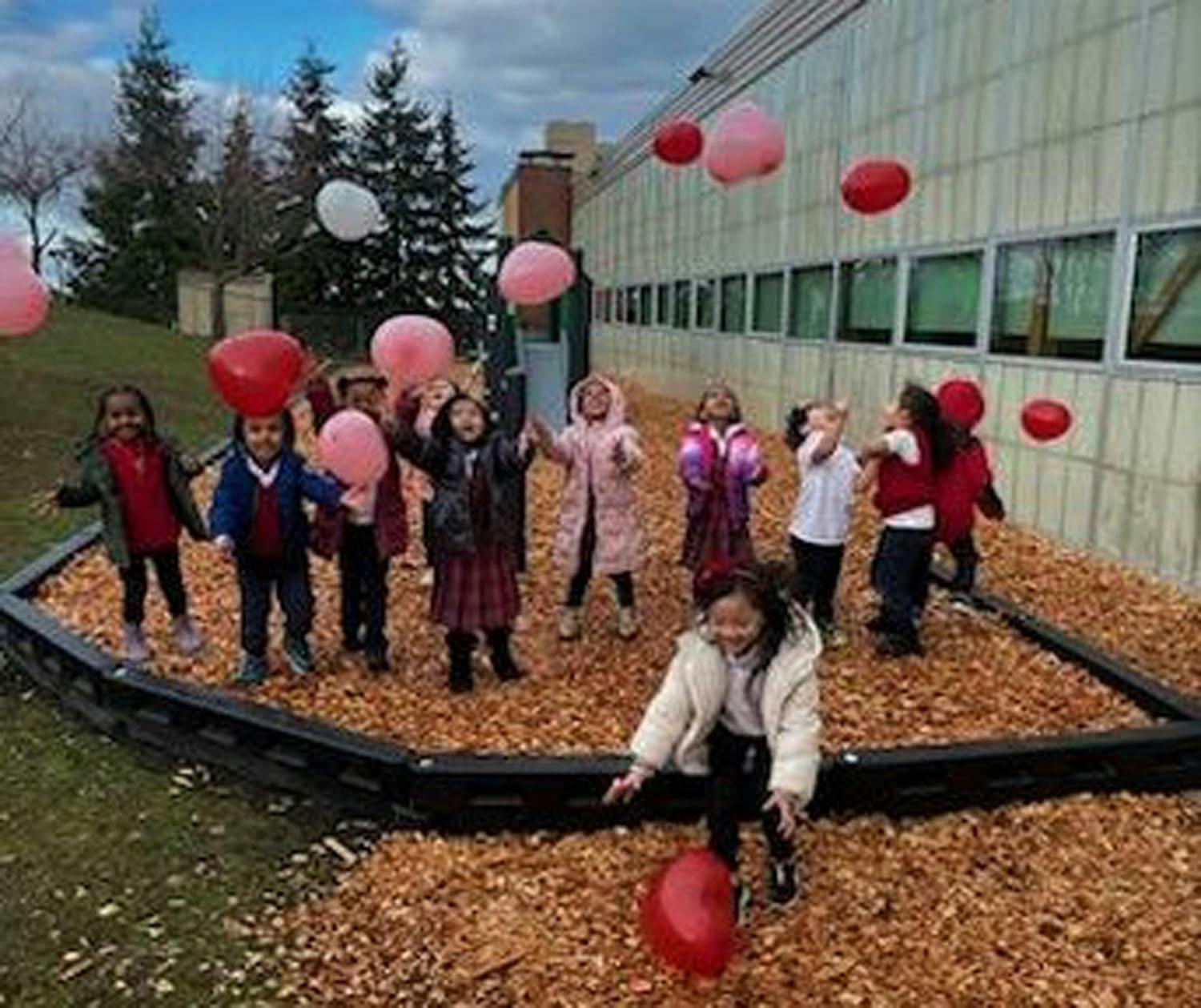 Group of children playing with red and pink balloons outdoors