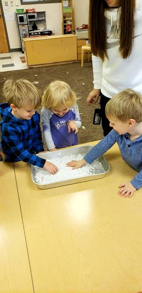 Three children playing with white powder in a tray on a table