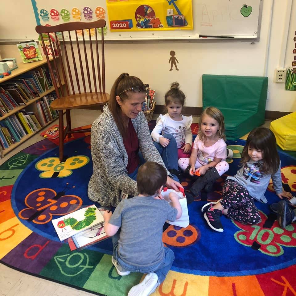 Adult and children sitting on a rug in a classroom