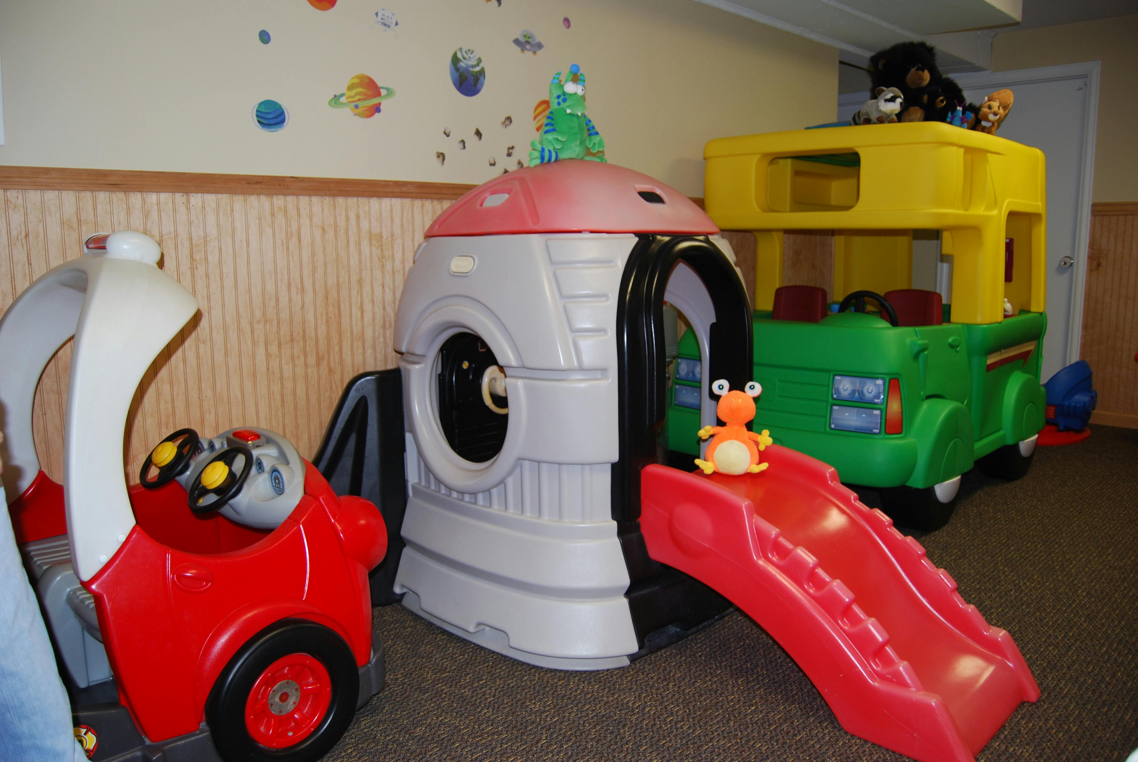 Indoor playground with a red toy car, a playhouse with a slide, and a toy bus