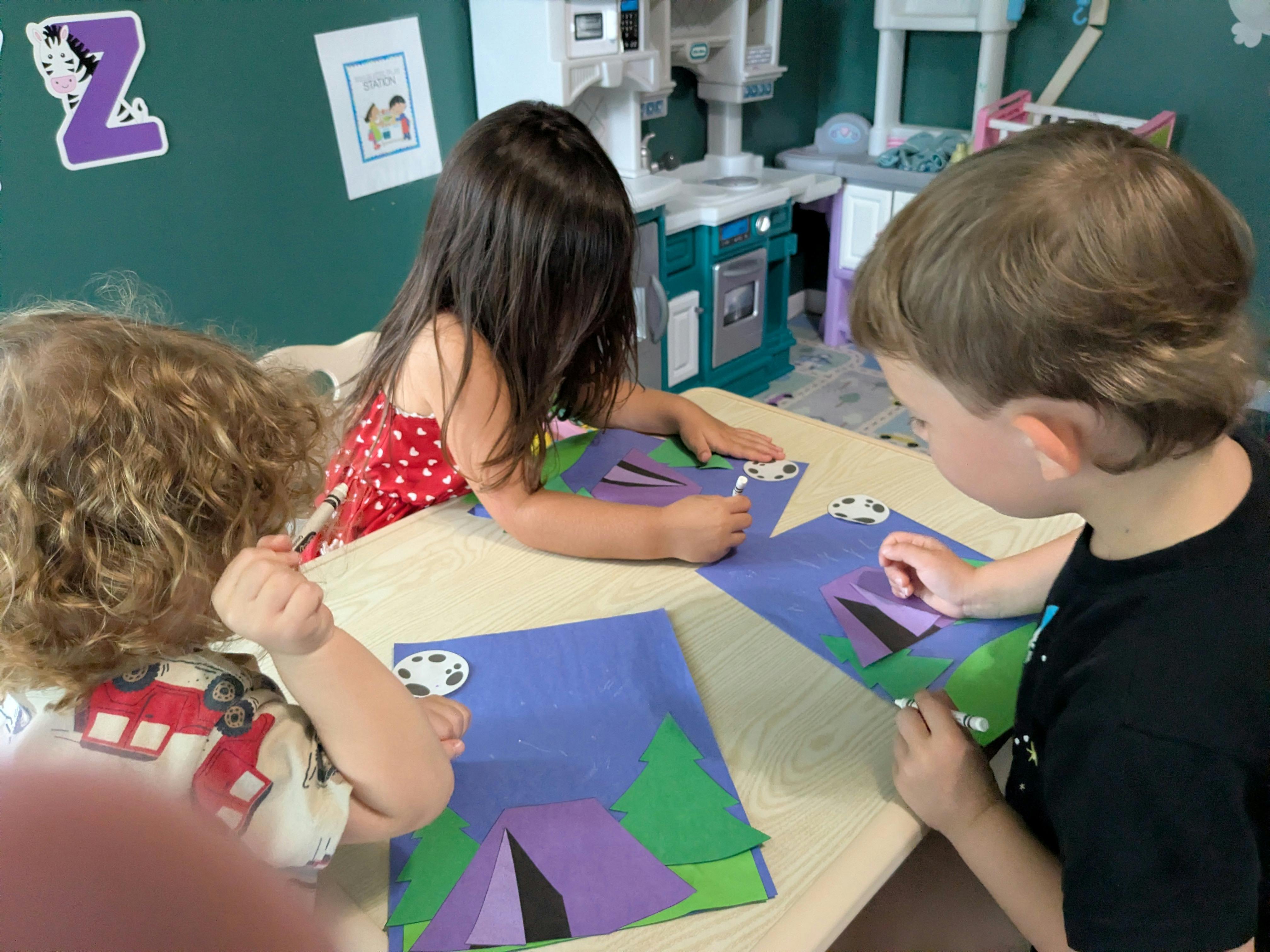 Three children working on construction paper crafts at a table