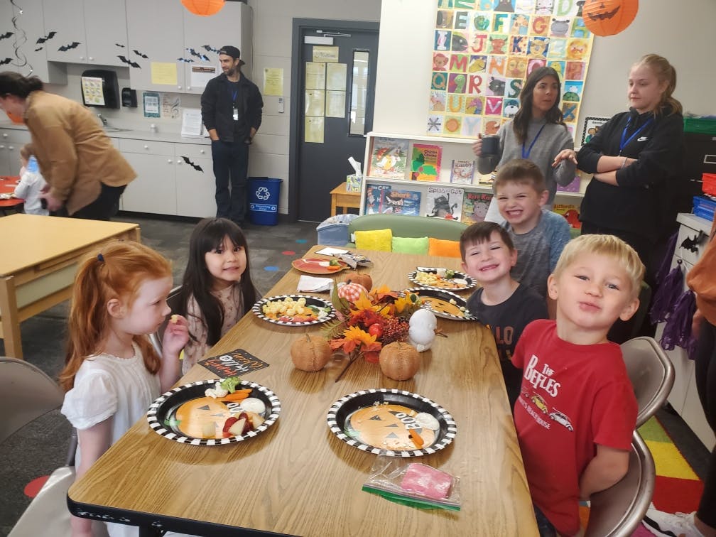 Children and adults in a classroom with decorated plates on plates on a table