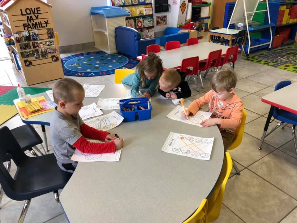 Children drawing and coloring at a table in a classroom
