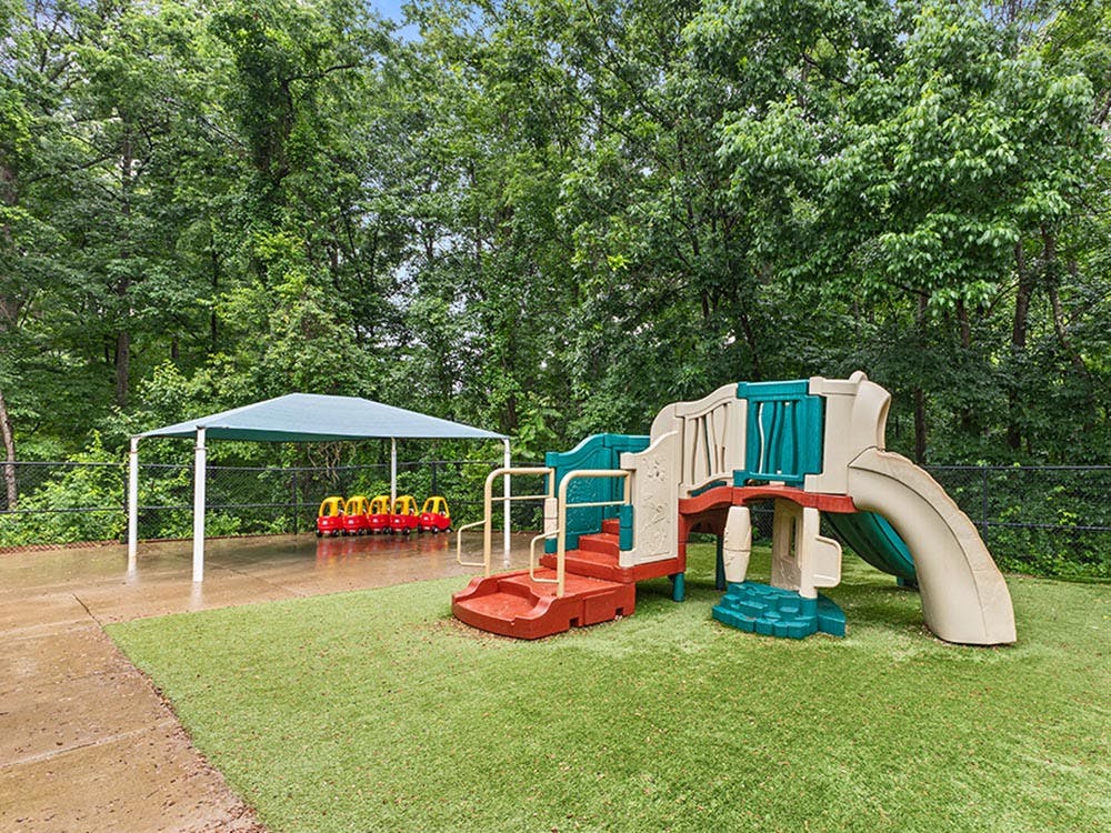 Playground with a play structure, slides, and covered area with small red cars