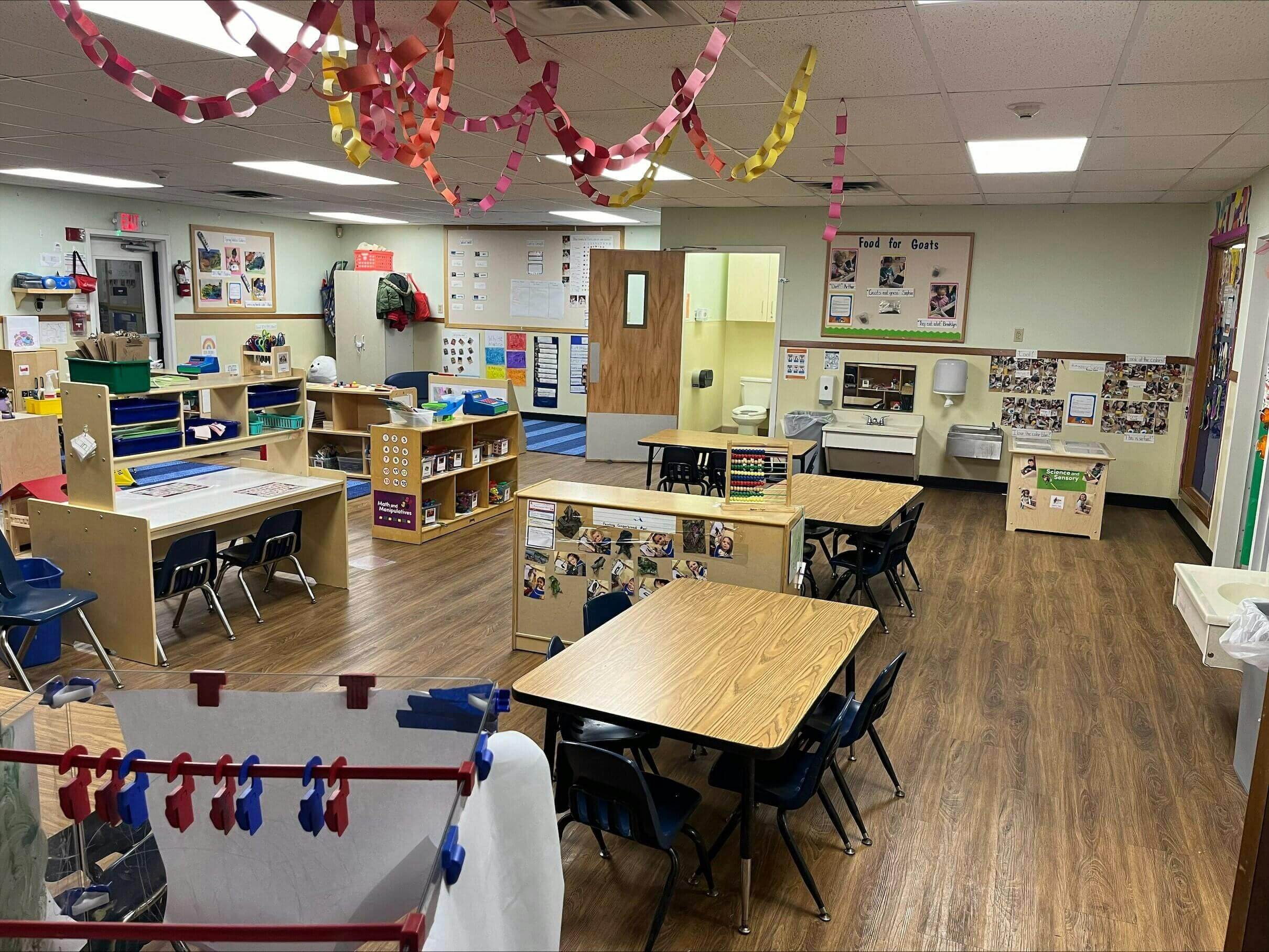 Classroom with child-sized tables and chairs, shelves with toys, and decorations