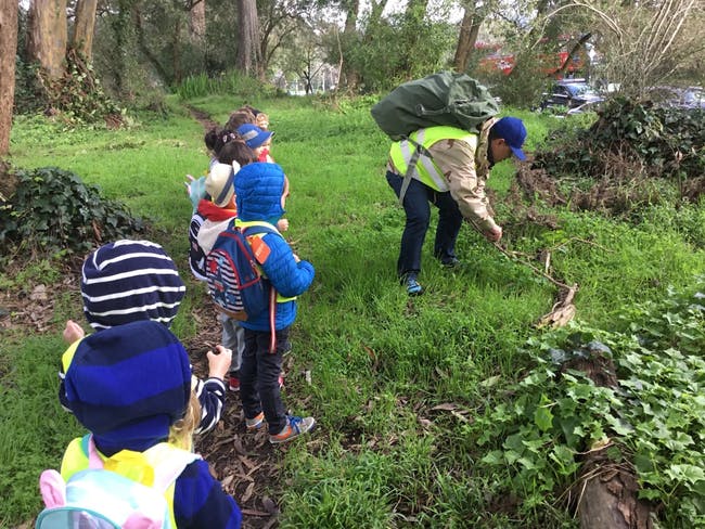 Person in a safety vest and children in a grassy area