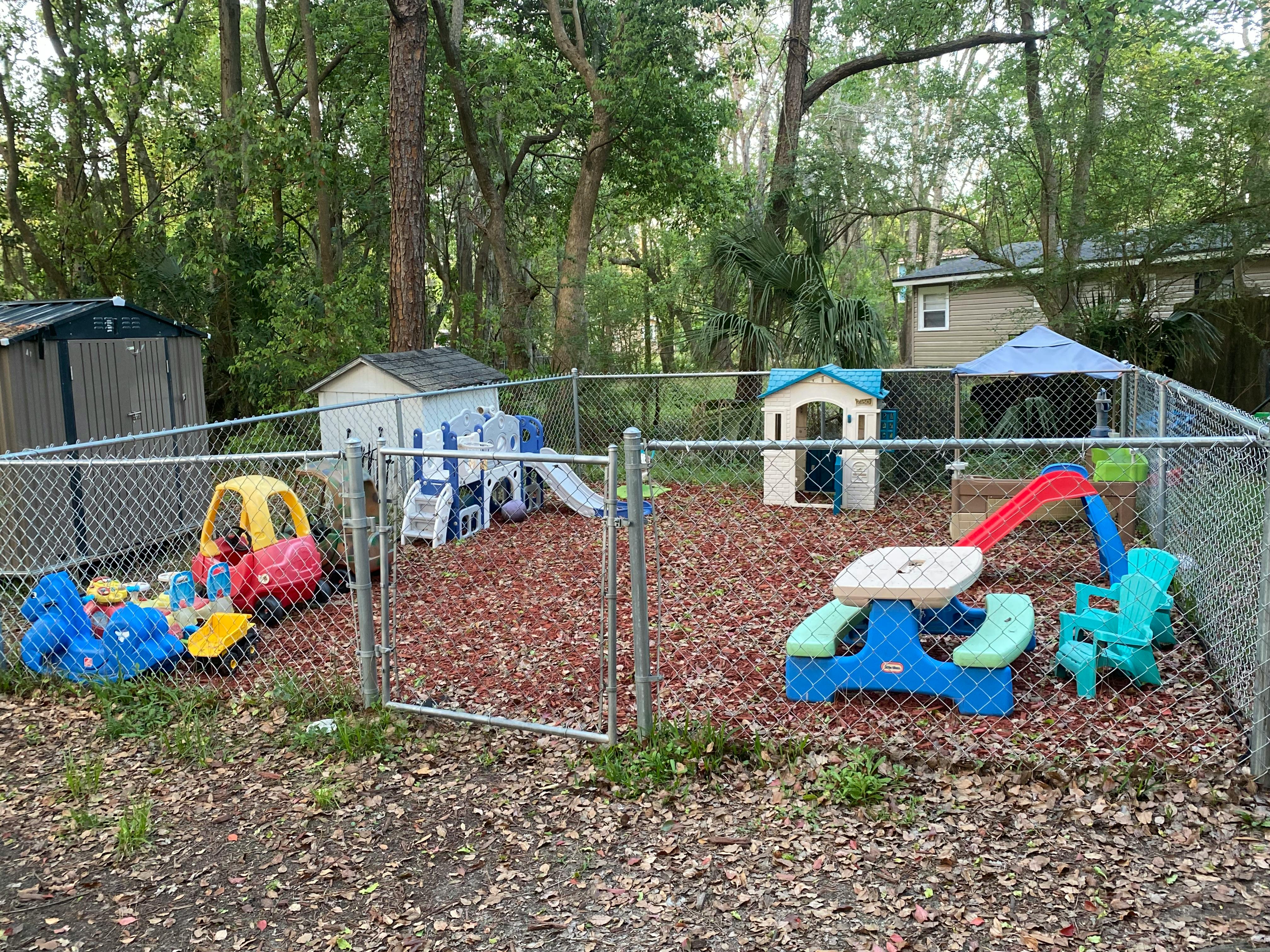Fenced outdoor play area with various colorful toys and wood chips