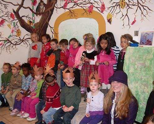 Group of children and one adult posing in front of a painted tree mural