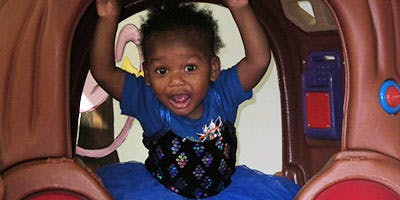 Child in a blue shirt and skirt playing in a brown play structure