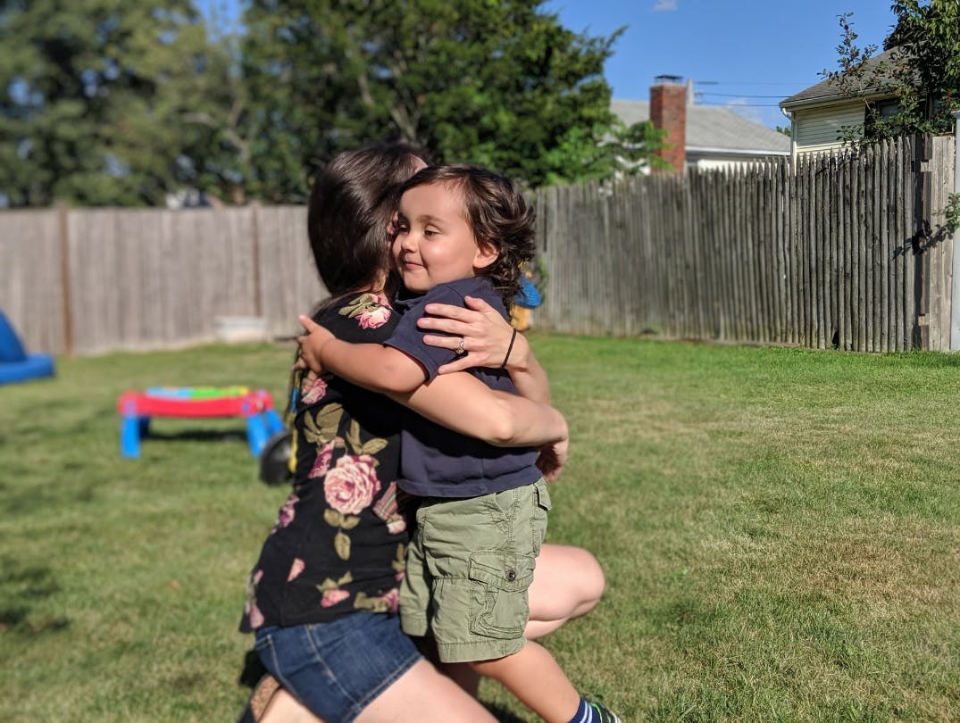Person hugging a child in a grassy yard
