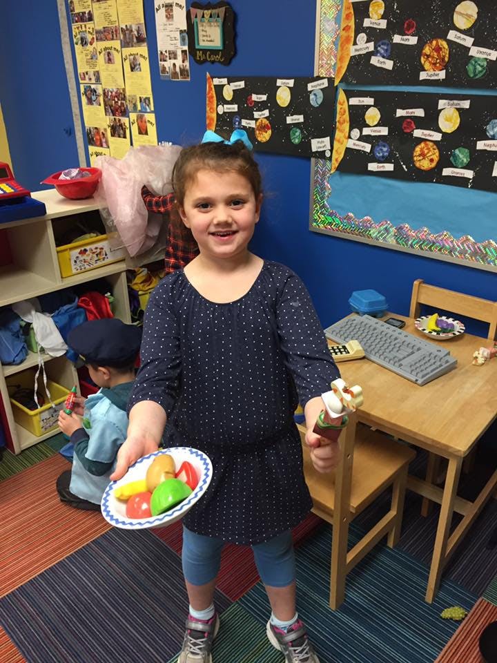 Child holding a plate of toy fruit and a toy ice cream cone