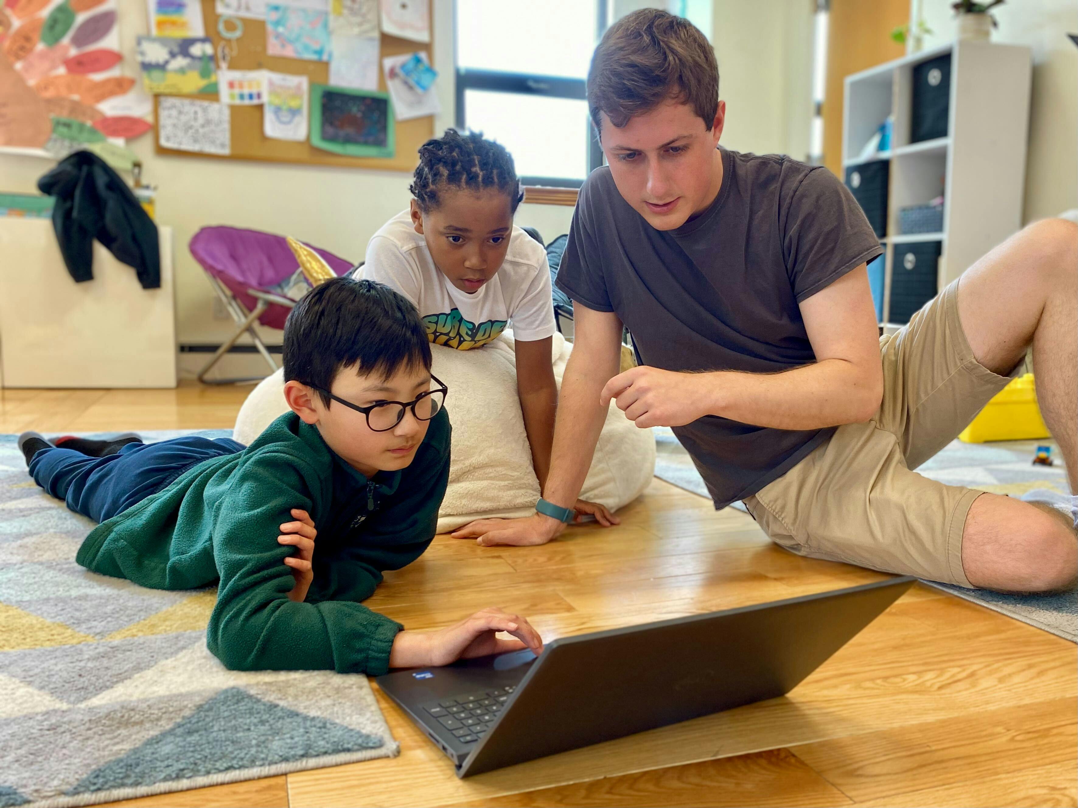 Adult and two children looking at a laptop on the floor