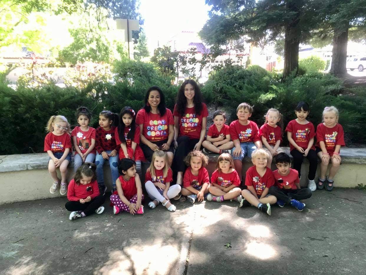 Two adults and many children in red shirts posing for a group photo outdoors