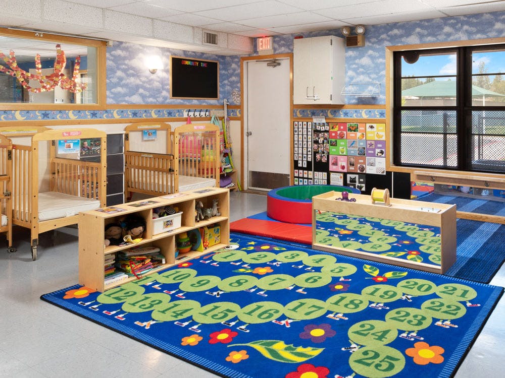 cribs in a daycare room with a colorful number rug on the floor