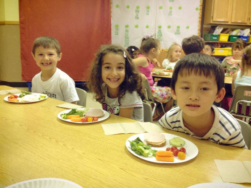 Three children sitting at a table with plates of food in a classroom