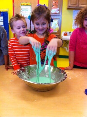 Child playing with green slime in a bowl