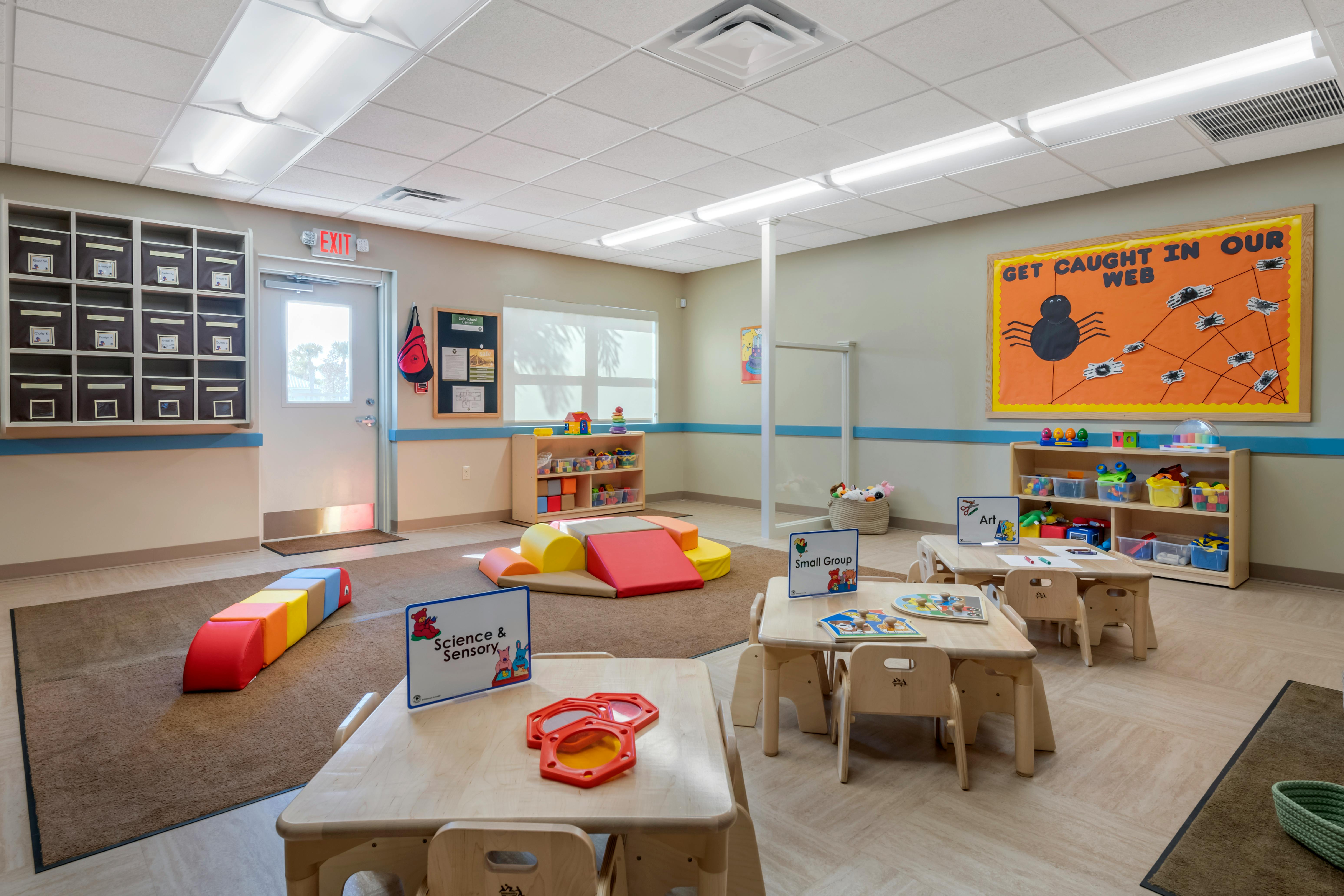 An empty early childhood classroom with various play areas and small tables