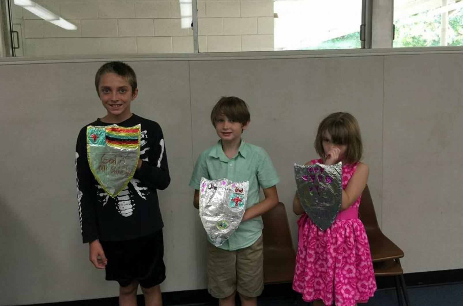 Three children holding up decorated masks