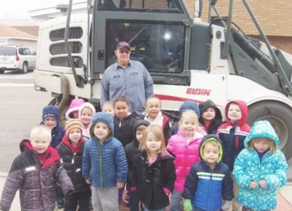 Person and group of children standing in front of a large vehicle